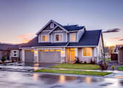 Thumbnail 1 of 5 - A house with a grey roof and a garage is shown.