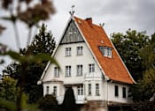 Thumbnail 2 of 5 - A white house with a red roof is surrounded by greenery.