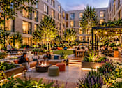 Thumbnail 5 of 6 - A group of people are sitting around a fire pit in a courtyard.