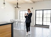 Thumbnail 1 of 10 - A woman in a black outfit is standing in a room with a wooden counter and a chandelier.