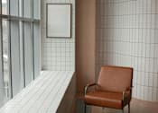 Thumbnail 4 of 10 - A brown leather chair sits in front of a wall with white tiles.