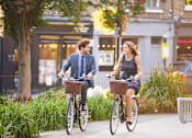 Thumbnail 1 of 21 - A man and a woman riding bicycles on a sidewalk.