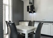 Thumbnail 1 of 5 - A white dining table with two black chairs in a modern kitchen.