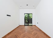Thumbnail 5 of 7 - A room with a wooden floor and a glass door leading outside.
