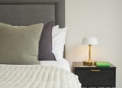 Thumbnail 16 of 29 - a bedroom with a bed and a nightstand with a lamp on it
