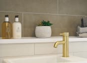 Thumbnail 14 of 29 - a white sink with a gold faucet and a white vase with a plant on
