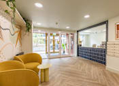 Thumbnail 20 of 25 - A hallway with yellow chairs and a blue tile wall.