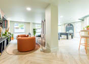 Thumbnail 2 of 25 - A living room with a large orange chair in the center.