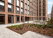 Thumbnail 18 of 36 - A courtyard with a brick building and a bench.