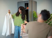 Thumbnail 31 of 54 - A woman holding a white shirt in front of a grey wardrobe.
