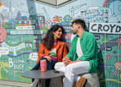 Thumbnail 45 of 54 - Two people sitting in front of a mural with the word "Croydon" on it.