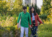 Thumbnail 51 of 54 - Two people walking through a green, leafy area.