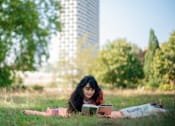 Thumbnail 50 of 54 - A woman is reading a book on a blanket in a grassy field.