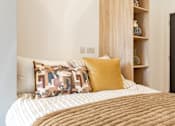 Thumbnail 30 of 35 - A bed with a white and tan comforter and two pillows with geometric patterns.