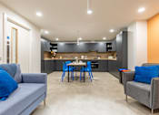 Thumbnail 19 of 35 - A modern kitchen with a grey couch and blue chairs.
