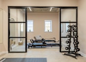 Thumbnail 61 of 65 - A gym with a row of dumbbells on the right and a row of bench presses on the left.