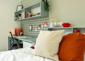 Thumbnail 18 of 36 - a bedroom with a bed with pillows and a desk with a chair