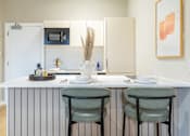 Thumbnail 51 of 65 - A kitchen with a white counter and two green chairs.