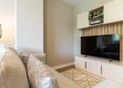 Thumbnail 62 of 65 - A living room with a couch, a television, and a cabinet with plants on top.