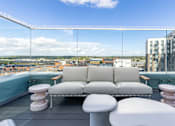 Thumbnail 15 of 41 - A white couch with a wooden table and two white stools are on a balcony with a glass railing.