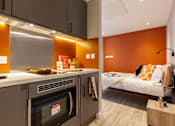 Thumbnail 22 of 36 - A modern kitchen with a built-in oven and a bedroom with orange walls in the background.
