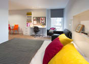 Thumbnail 1 of 16 - a bedroom with a bed and a desk with a chair