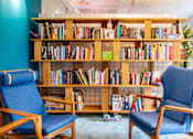 Thumbnail 21 of 51 - Two blue chairs are in front of a bookshelf filled with books.