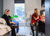 Thumbnail 33 of 51 - Two women sitting in a room with a window in the background.