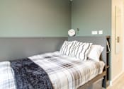 Thumbnail 45 of 51 - A bed with a plaid comforter and striped pillows in a room with green walls.