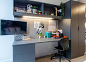 Thumbnail 43 of 51 - A modern home office with a grey desk, black chair, and shelves with various items.