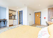 Thumbnail 6 of 41 - A bedroom with a bed in the foreground and a kitchen area in the background.
