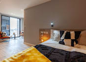 Thumbnail 11 of 36 - A bedroom with a bed, a yellow blanket, and a window with blinds.