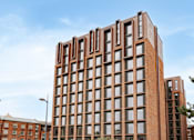 Thumbnail 35 of 36 - A tall red brick building with many windows stands in front of a blue sky.