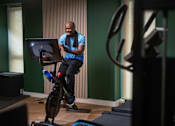 Thumbnail 46 of 85 - A man is exercising on a stationary bike in a room.