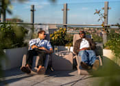Thumbnail 19 of 85 - Two men are sitting on chairs on a rooftop terrace.