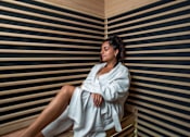 Thumbnail 13 of 85 - A woman in a white robe is sitting in a sauna.