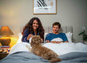 Thumbnail 78 of 85 - A man and woman are sitting on a bed with a dog.