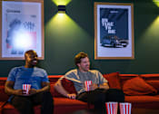 Thumbnail 4 of 85 - Two men sitting on a couch with popcorn and watching a movie.