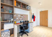 Thumbnail 16 of 29 - A room with a desk, chair, and shelves with various items.