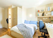 Thumbnail 19 of 35 - A bedroom with a bed, desk, and chair.