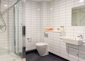 Thumbnail 14 of 19 - A white tiled bathroom with a toilet, sink, and shower.