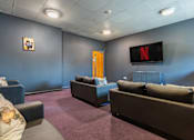 Thumbnail 28 of 30 - A living room with a couch, chair, and a television displaying the Netflix logo.
