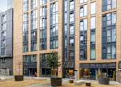 Thumbnail 47 of 49 - A modern building with a black and brown facade and a courtyard with trees and benches.