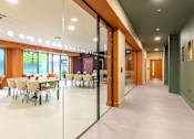Thumbnail 19 of 49 - A long hallway with tables and chairs on the left side.
