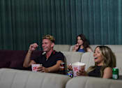 Thumbnail 21 of 49 - A group of people are sitting in a movie theater watching a movie on a large screen.