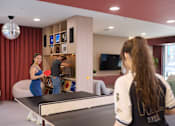 Thumbnail 48 of 49 - Two women playing ping pong in a room with red curtains.