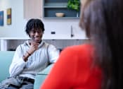 Thumbnail 23 of 49 - A man with dreadlocks is sitting on a green couch and smiling at a woman in a red top.