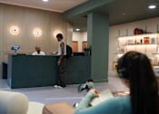 Thumbnail 26 of 49 - A reception area with a woman standing at the desk and a man sitting down.