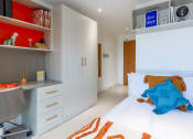 Thumbnail 29 of 49 - a bedroom with white walls and a white bed with an orange and blue blanket