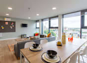 Thumbnail 19 of 51 - Shared flat kitchen, with wall-mounted television, large sofa and dining table with chairs, decorated with plates and bowls.